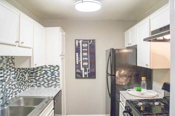 A kitchen with a black fridge and a black and white tiled backsplash.
